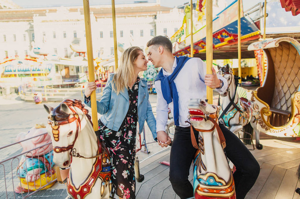 young couple sitting on carousel horses and kissing - Zdjęcie, obraz