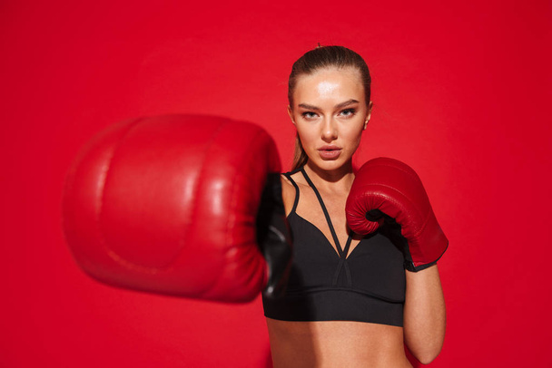 Image of a beautiful young fitness boxer woman posing isolated over red wall background make exercises in gloves. - Zdjęcie, obraz