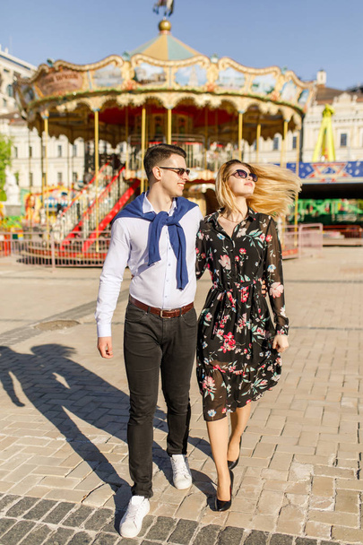 happy couple walking by carousel in bright sunlight - Photo, Image