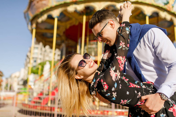 happy couple posing by carousel in bright sunlight - Фото, изображение