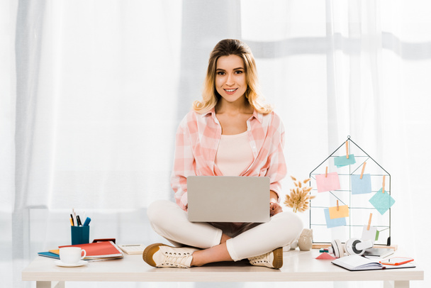 Smiling woman in checkered shirt sitting on table with laptop - Foto, Bild