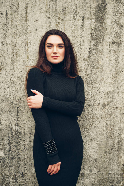 Outdoor portrait of young 35 year old woman with long dark hair, wearing black turtle neck dress - Photo, Image