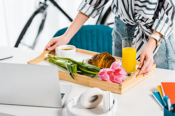 Vista parcial de la mujer sosteniendo bandeja con desayuno en el lugar de trabajo
 - Foto, Imagen