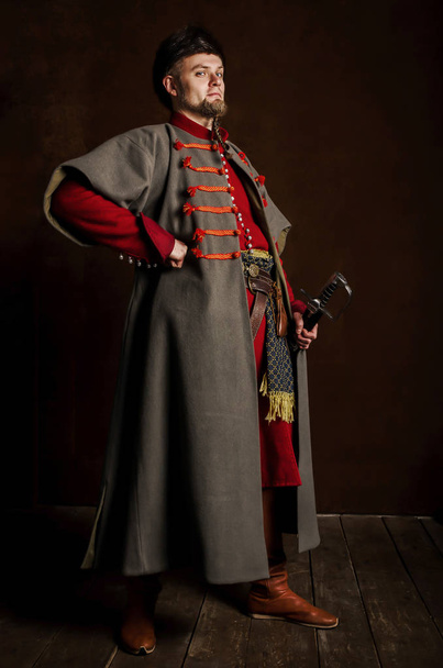 暗い背景に中世の衣装で男の肖像画。ポーランドの貴族の服。誇りを持って、厳格な男は歴史的衣装から始まります - 写真・画像