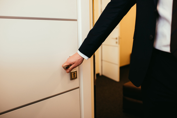 partial view of man holding door handle and coming into hotel room - Foto, afbeelding