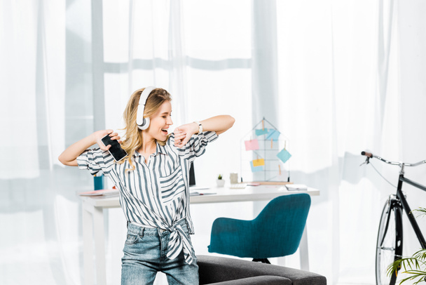 Carefree girl in striped shirt dancing and listening music in headphones - Photo, Image