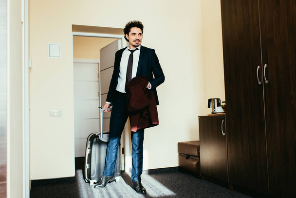 ホテルの部屋でスーツケースにスーツのビジネスマン - 写真・画像