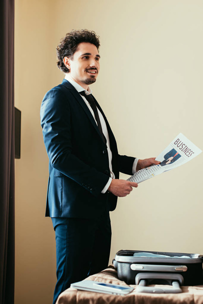 бізнесмен тримає ділову газету біля ліжка з багажем в готельному номері
 - Фото, зображення