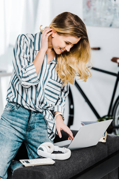 Charming young woman in striped shirt using laptop at home - Foto, afbeelding