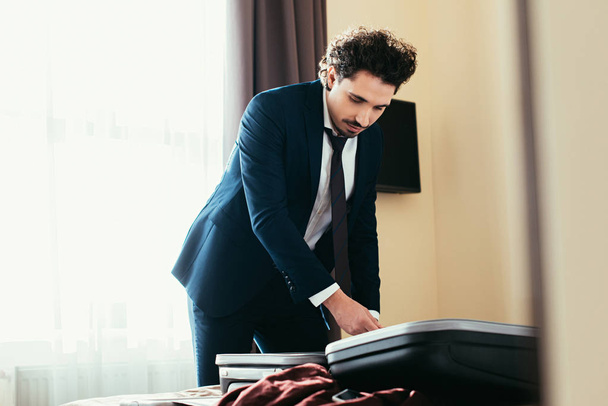 handsome businessman with travel bag on bed in hotel room   - Foto, imagen