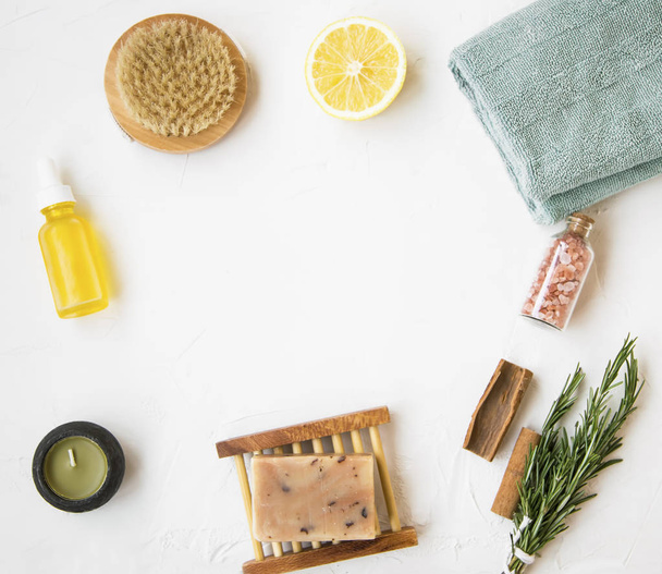 Organic skincare products flatlay with natural soap, oil bottle, brush, candle, salt, towel, rosemary herb, lemon and cinnamon, clean minimalist grey concrete background with copy space - Photo, Image