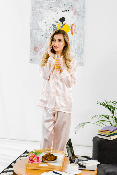 Smiling woman in pyjamas talking on smartphone and drinking orange juice in morning - Foto, Imagem