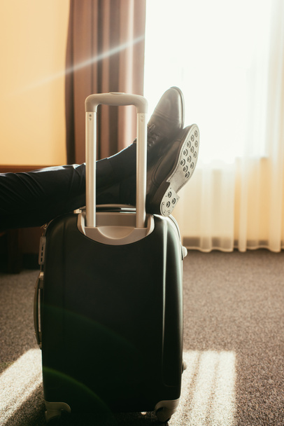 cropped view of man with legs on travel bag in hotel room - Fotoğraf, Görsel