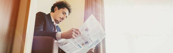 handsome businessman in suit reading newspaper in hotel room with sunlight - Photo, Image