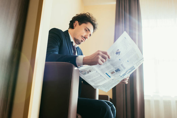 businessman in formal wear reading newspaper in hotel room with sunlight - Фото, изображение
