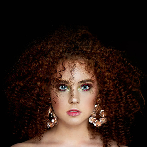 A girl with lush curly red hair. Close face with bright make-up and massive earrings. Purple shadows. - Foto, Imagem