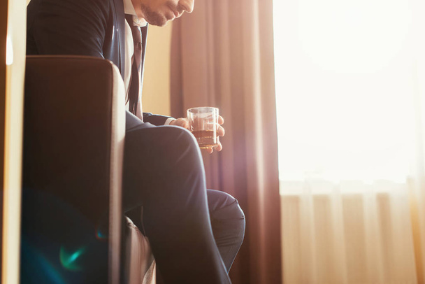 Ausgeschnittene Ansicht eines aufgebrachten Geschäftsmannes in offizieller Kleidung, der ein Glas Whiskey im Hotelzimmer hält  - Foto, Bild