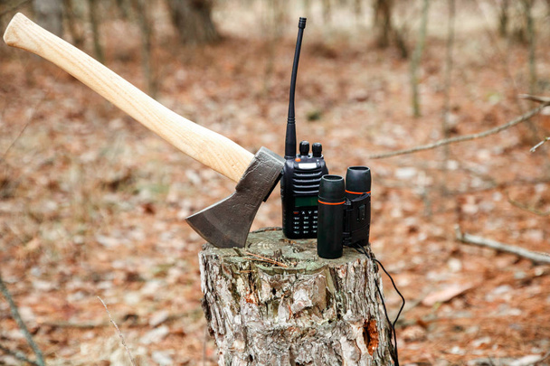 hacha, prismáticos y radio colocados en el muñón en el bosque de otoño
 - Foto, imagen