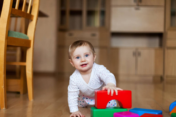  μωρό παίζει με πλαστικούς κύβους στο πάτωμα στο δωμάτιο.  - Φωτογραφία, εικόνα