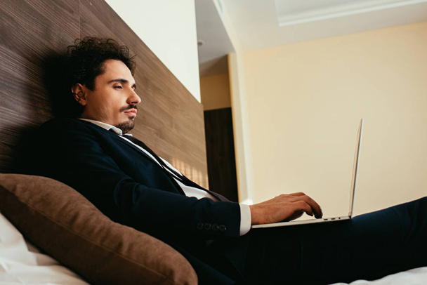homme d'affaires en costume télétravail sur ordinateur portable dans la chambre d'hôtel
 - Photo, image