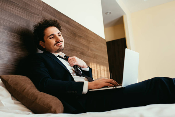 tired businessman in suit working on laptop in hotel room - Photo, Image