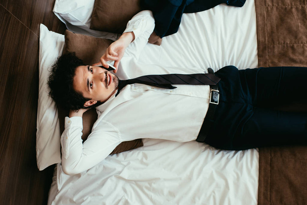 businessman lying on bed and talking on smartphone in hotel room - Photo, Image