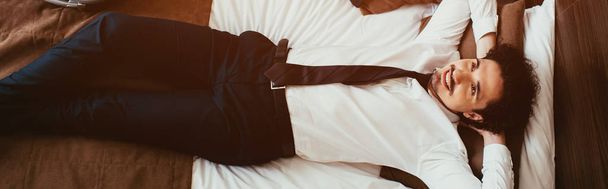 top view of smiling businessman relaxing on bed in hotel room - 写真・画像