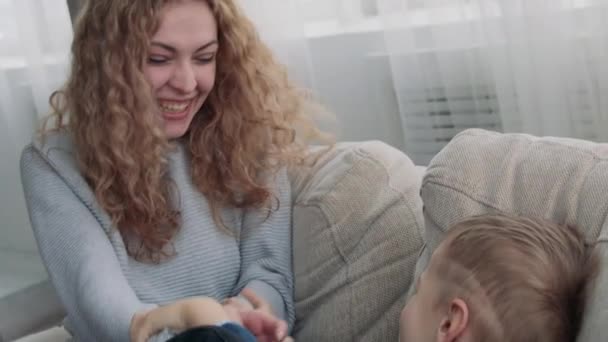 Mom tickles son on the couch - Materiał filmowy, wideo