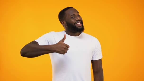 Young bearded black guy giving thumbs up, smiling at camera on yellow background - Materiał filmowy, wideo