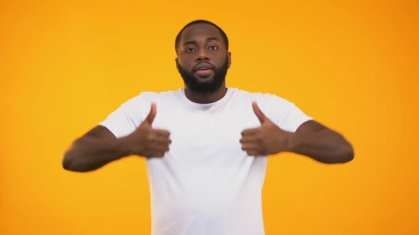 Handsome black man smiling confidently, showing thumbs up on yellow background - Video