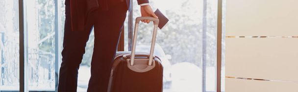обрезанный вид бизнесмена с паспортом и багажом, приходящего в отель с солнечным светом
 - Фото, изображение