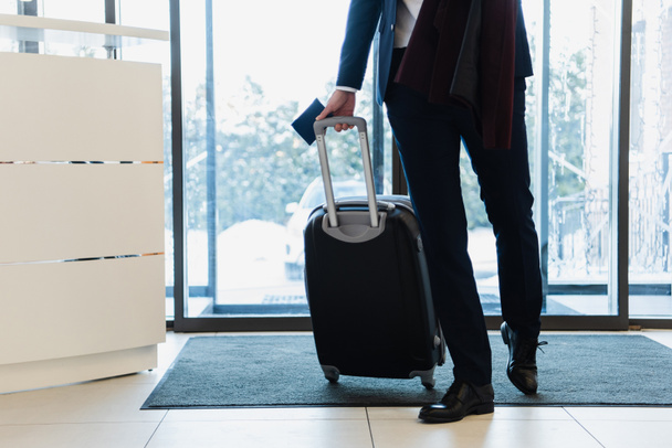 oříznutý pohled podnikatel s pas a cestovní taška přichází do hotelu  - Fotografie, Obrázek