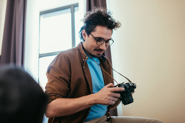 Mann mit Brille blickt in Hotelzimmer auf Fotokamera - Foto, Bild