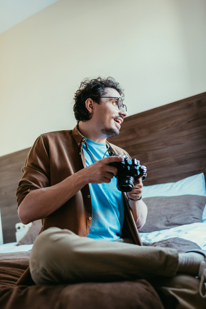 szczęśliwy człowiek w okularach, trzymając aparat fotograficzny w pokoju hotelowym - Zdjęcie, obraz