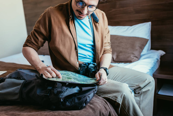 handsome traveler in eyeglasses looking at map in hotel room - Foto, immagini