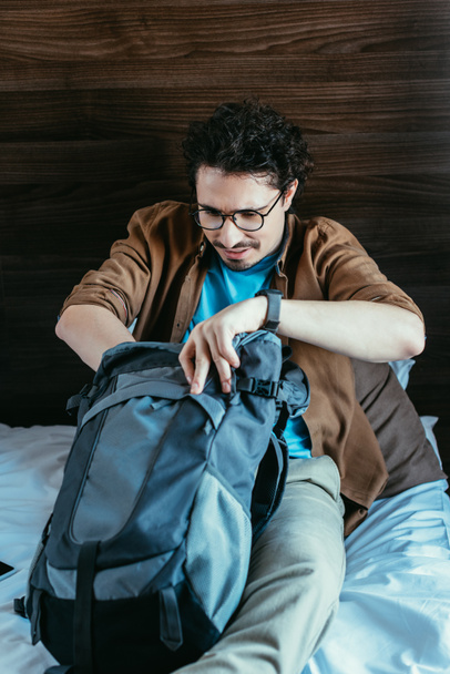 mężczyzna podróżnik biorąc coś z plecaka w pokoju hotelowym - Zdjęcie, obraz