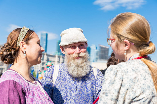 モスクワ、ポクロンナヤの丘公園、2018 年 7 月 11 日: 2 人の若い女性とグレー口ひげとあごひげのロシアの民族衣装と笑顔の老人が立っています。老いも若き - 写真・画像