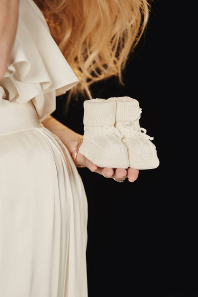 Беременная женщина с маленькими кроссовками в руках
 - Фото, изображение