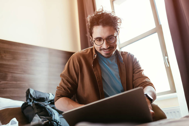 mosolygó férfi utas használ laptop a szállodai szobában a hátizsák - Fotó, kép
