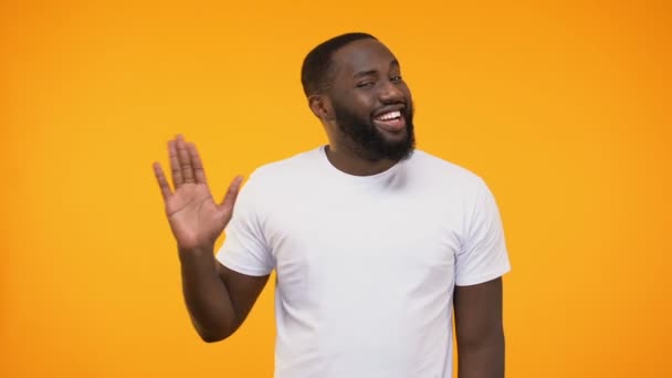 Affable young black man waving hand neighborly, isolated on yellow background - Video