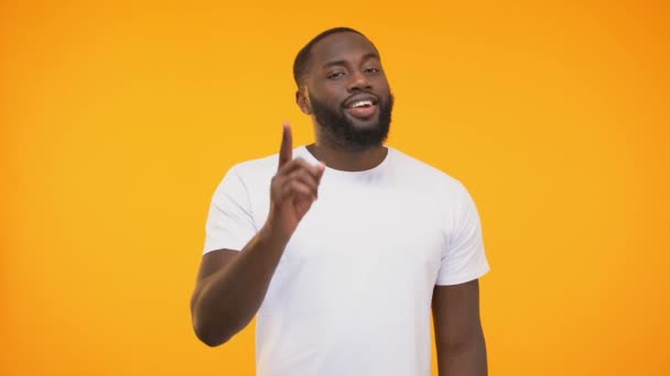 Smiling black man pointing finger, winking knowingly against yellow background - Filmati, video
