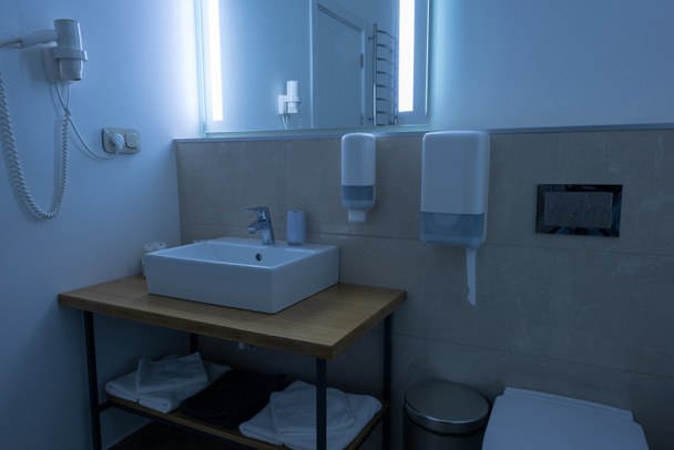badkamer met wastafel, toilet, handdoeken en een föhn - Foto, afbeelding
