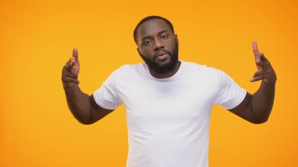 Angry black male throwing finger guns at camera, isolated on yellow background - Metraje, vídeo