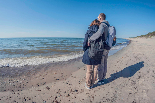Loving couple watching the sea in winter on a sunny day, hugging each other - Fotoğraf, Görsel