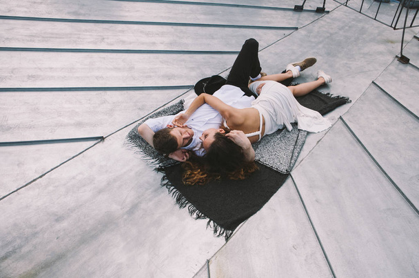 couple in love lying on the roof of the house and hugging - a girl in a white dress and a guy with a hat - positive and sincere emotions of love - Foto, Imagen