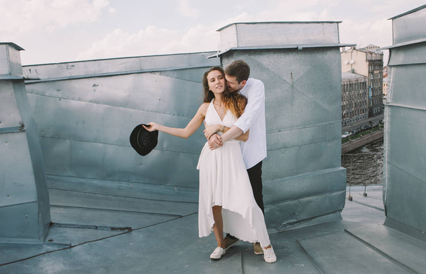 loving couple - a girl in a white dress and a guy with a hat - on a walk on the roof hugging and laughing,  positive and sincere emotions of love - Fotó, kép
