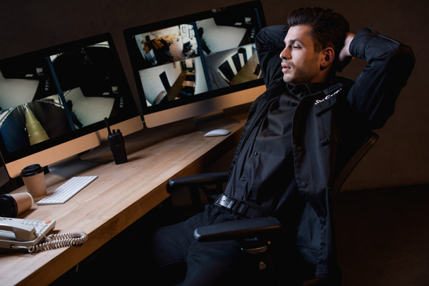  guardia en uniforme con brazos cruzados mirando el monitor de la computadora
  - Foto, Imagen