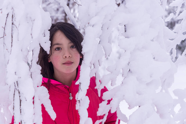 Joven chica asiática de pie detrás de las ramas cubiertas de nieve en chaqueta rosa
 - Foto, Imagen