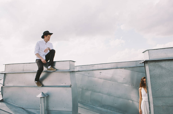 loving couple - a girl in a white dress and a guy with a hat - on a walk on the roof hugging and laughing, a view from the roof of the city, positive and true emotions of love  - Photo, image