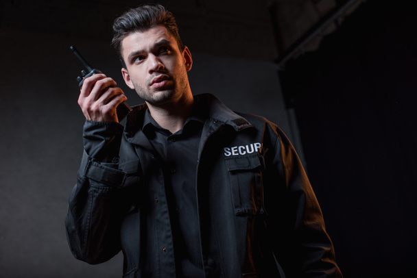 guard in black uniform holding walkie-talkie and looking away  - Foto, afbeelding